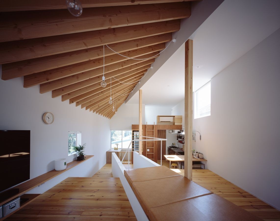 スキップフロアの大空間の中に斜めに階段を配置し、緩やかに空間が仕切られています。周辺の緑へ向けた開口部に合わせて屋根の軸線を傾けることで屋根がねじれ、垂木に導かれて視線が緑へ向かいます。階段上部はデイベッドになっています。Photo by Masao Nishikawa | スキユハウス　―犬と暮らす、ねじれ屋根の家―